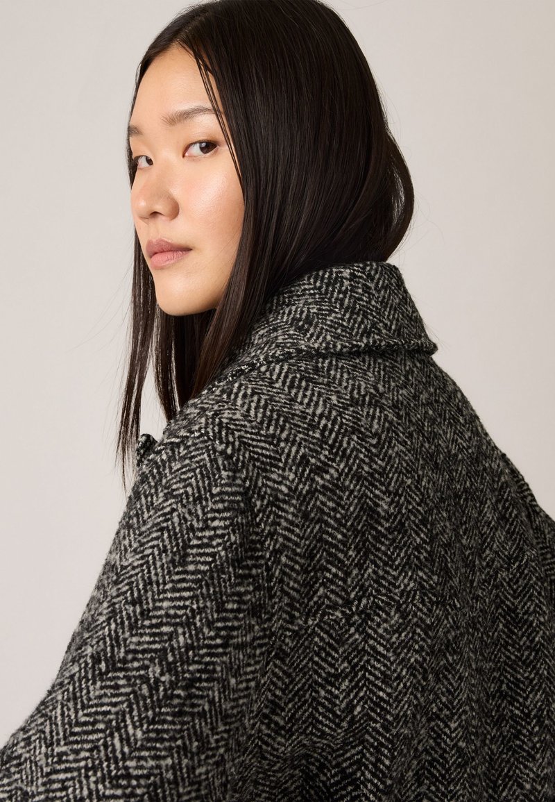 Grauer Fischgrät-Wollmantel mit strukturiertem Kragen und texturiertem Muster, ausgestattet mit einer lässigen Silhouette und seitlichem Knopfverschluss.
