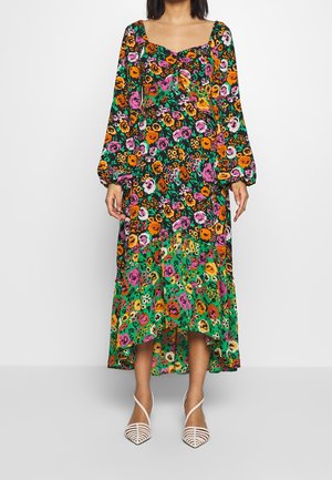 Woman wearing a long floral dress with pink, orange, and yellow flowers, puffed long sleeves, and white pointed strappy heels.