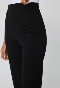 Zwarte broek met een gladde textuur, voorzien van een hoge tailleband, rechte snit en scherpe plooien voor een verzorgde uitstraling.