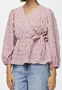 Top floreale rosa avvolgente con maniche a palloncino, tessuto texturizzato e vita legata. Abbinato a jeans denim azzurri.