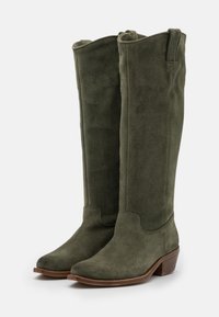 Botas de ante verde oliva hasta la rodilla, con puntera redondeada, un pequeño tacón y una textura suave con un mínimo detalle de costura.