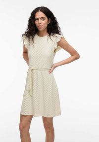 Cremfarbendes Kleid mit tailliertem Schnitt, ausgestellt kurzen Ärmeln und einem V-förmigen Lochmuster. Mit Bändern an der Taille zur Anpassung.