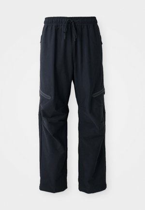 Pantalones casuales negros con cinturilla elástica, cordón y bolsillos con cremallera sobre un fondo blanco.