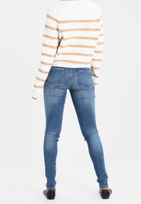 Jeans pitillo de mezclilla azul claro con una textura suave. Combinados con un suéter a rayas blancas y beige. Zapatos planos visibles.