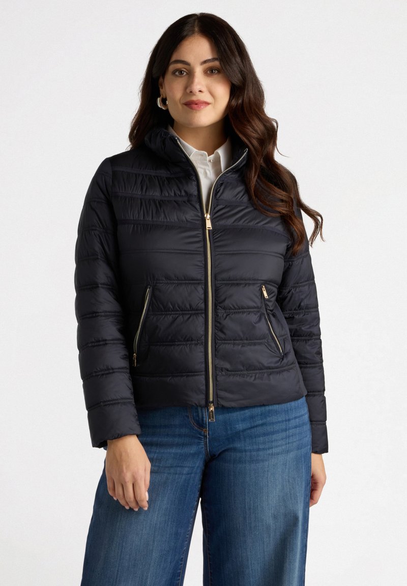 Chaqueta acolchada azul marino con cuello alzado, cierre de cremallera y dos bolsillos delanteros. Presenta costuras horizontales y acentos en tono dorado.