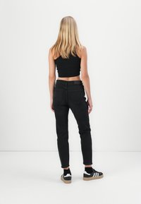 Sorte høyt liv jeans vist fra baksiden, kombinert med en svart cropped topp og svart-hvite joggesko med gummisåle.