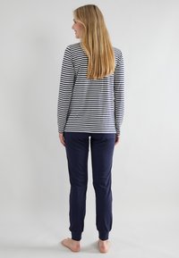 Blusa de manga larga a rayas en azul marino y blanco, combinada con pantalones azul marino. La blusa presenta un escote redondo; los pantalones tienen puños elásticos. Modelo visto desde atrás.