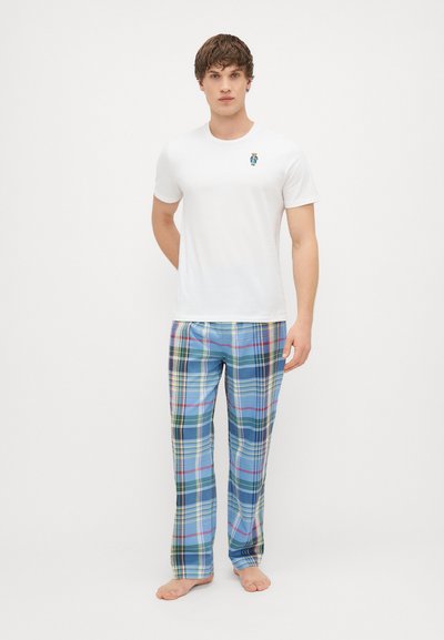 Balts īsām piedurknēm krekls ar mazu zilu un zaļu izšuvumu, apvienots ar ziliem pārbaudītiem biksēm, kurām ir zaļas, dzeltenas un sarkanas akcenti.