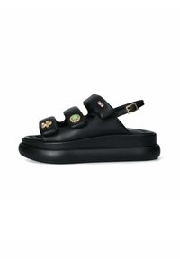 Black sandal with three padded straps, adorned with decorative stones in green and gold. Features a back strap and thick sole.