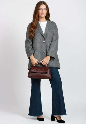 Cappotto di lana grigio con colletto a rever e due bottoni, abbinato a jeans blu svasati e borsa bordeaux. Scarpe nere completano l'outfit.