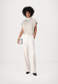 Lichtgrijze korte mouwen top, witte op maat gemaakte broek en zwarte schoenen. Zilveren handtas met een trekkoordaccent. Gladde texturen, modern ontwerp.
