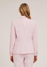 Blazer rosa su misura con design a doppio petto, colletto a punta e polsini con bottone. Tessuto liscio con vestibilità strutturata e spacco posteriore.