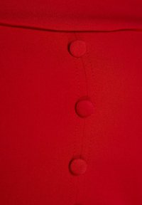 Gros plan d’un tissu rouge avec trois boutons recouverts alignés verticalement et un bord plié en haut.