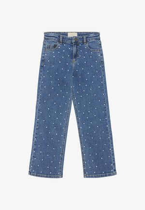 Chaqueta vaquera con detalles de perlas, cierre de botones y mangas largas. Se lleva con una camiseta blanca de canalé y jeans, mostrando un look casual.