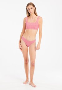 Ručno izrađeni ružičasti bikini set s prugama, koji se sastoji od gornjeg dijela s kvadratnim izrezom i širokim trakama, te odgovarajućih donjih dijelova s niskim strukom. Mekana tekstura, lagana tkanina.