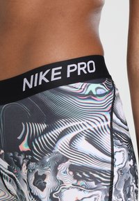 Cintura y cadera de una persona que lleva leggings con un patrón abstracto multicolor y una cinturilla negra etiquetada "NIKE PRO".