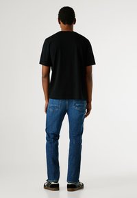 Černé bavlněné tričko a modré džíny. Tričko má kulatý výstřih; džíny mají klasický střih s viditelnými zadními kapsami. Černé boty dokončují vzhled.