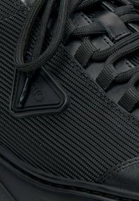 Černé tenisky s texturou síťoviny, robustními tkaničkami a trojúhelníkovým gumovým logem. Design zdůrazňuje lehkou a prodyšnou konstrukci.