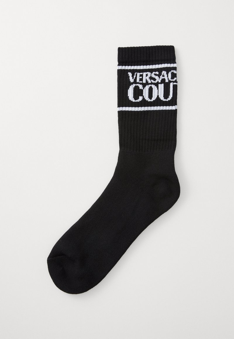 Black knit sock with ribbed top, featuring white "VERSACE COURT" text framed by a white stripe. Smooth texture, mid-calf length.