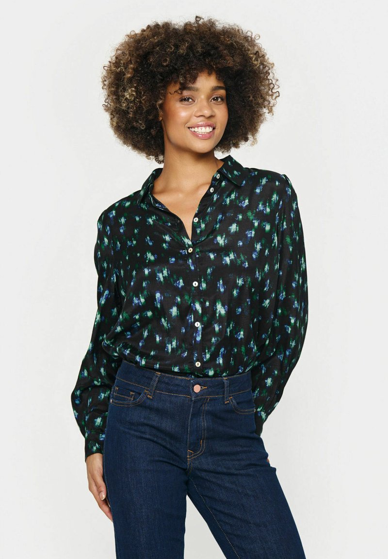 Camisa negra de botones con un patrón abstracto en verde y azul, de mangas largas y corte relajado, combinada con jeans azules oscuros.