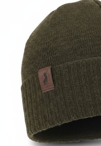 Olive green knitted beanie with a ribbed pattern and a brown leather logo patch featuring a stag silhouette. Soft texture and fold-over design.