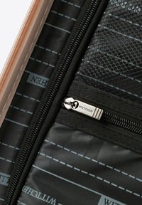 Nahaufnahme einer schwarzen Innentasche eines Koffers mit einem Metall-Reißverschlussanhänger, der "WITTCHEN" eingraviert hat, und einem Detail aus Netzstoff.