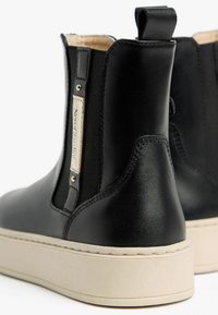Bottes de cheville en cuir noir avec des panneaux latéraux élastiques, semelles en caoutchouc beige et une languette à l'arrière. Présente une étiquette de marque sur le côté.