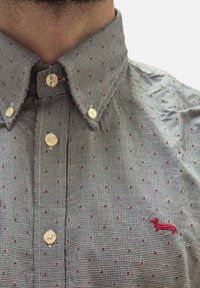 Camicetta button-down a scacchi neri e bianchi con piccoli punti rossi; presenta un logo ricamato di un bassotto rosso sul petto.