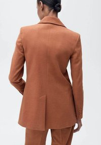 Blazer marron texturé avec un col cranté, une fente simple et des détails de poignet boutonné. Design simple sans embellissements ni motifs visibles.