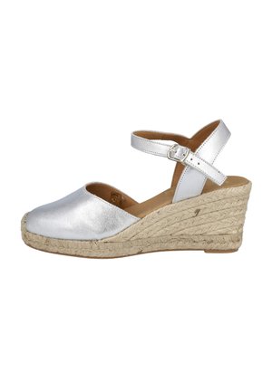 Sandalia cuña de cuero plateado con correa de tobillo con hebilla y suela de yute trenzado sobre fondo blanco.