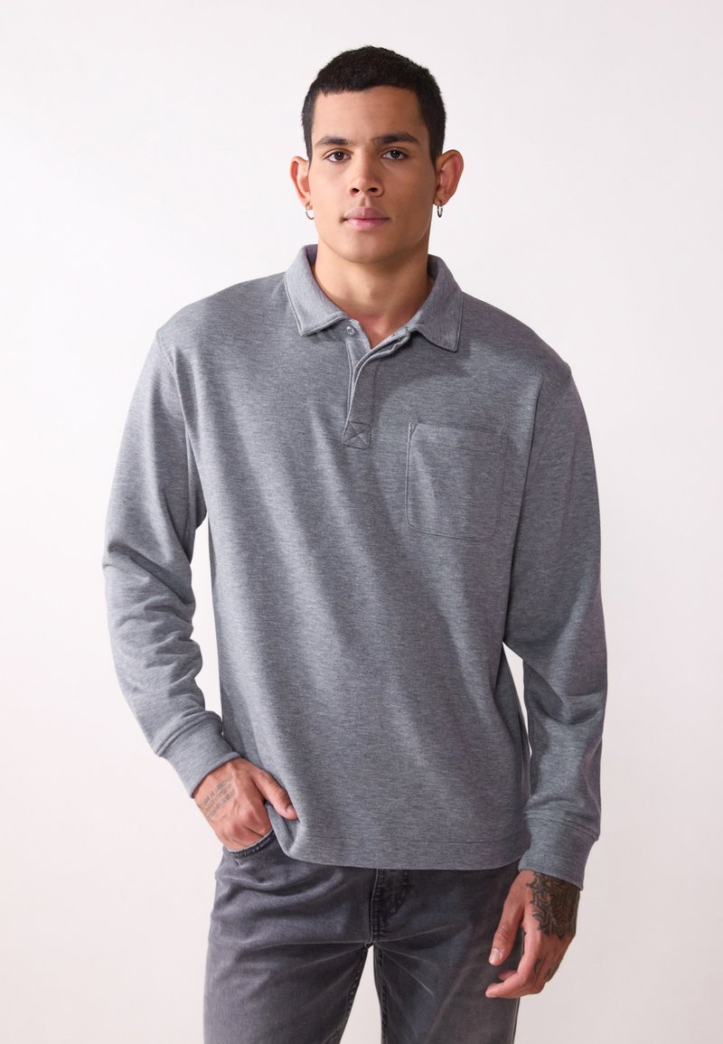 Polo grigio a maniche lunghe con colletto, taschino sul petto e orlo dritto. Tessuto morbido con una leggera trama e design aderente.