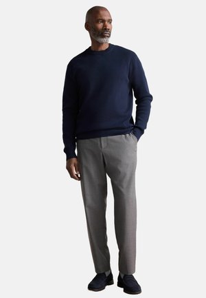 Pull en maille marine, pantalon gris ajusté et chaussures marines. Texture lisse, coupe décontractée, design minimaliste, col et poignets côtelés.