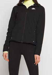 Black zip-up jacket made of soft fabric, featuring a white Nike logo, high collar, and contrasting lime green inner collar and cuffs.
