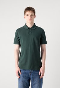 Mørkegrønn polo skjorte laget av bomull, med klassisk krage, to-knapp placket og kortermede ermer. Diskret logo på brystet.