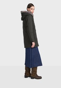 Czarna parka z futrzanym kapturem, o prostym kroju i długich rękawach. Zestawiona z długą niebieską spódnicą dżinsową i brązowymi skórzanymi botkami.