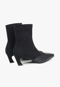 Czarne botki do kostki wykonane z zamszu i skóry, z wąskim noskiem i niskim, rozszerzanym obcasem. Gładka faktura z kontrastowymi akcentami.