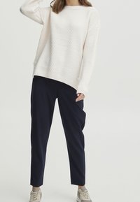 Maglione dalla texture cremosa con orlo a coste, abbinato a pantaloni affusolati blu navy e sneakers grigio chiaro. Design di outfit semplice e casual.