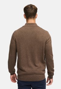 Pull en maille marron avec un col montant, des poignets côtelés et un ourlet. Le tissu semble doux avec une finition texturée.