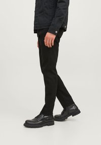 Botas de cuero negras hasta el tobillo con suela de goma, combinadas con pantalones negros ajustados y una chaqueta negra. La textura parece suave con un acabado mate.