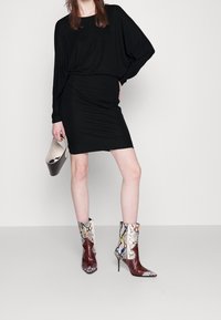 Czarna sukienka z długim rękawem o dopasowanej sylwetce, zestawiona z wielokolorowymi botkami w wężowy wzór i małą brązową torebką.