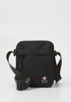 Black crossbody bag made of durable fabric, featuring a top zipper closure, adjustable strap, and a small Champion logo patch on the front.