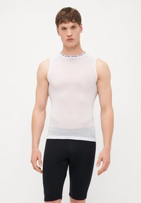 Haut sans manches en maille blanc avec col rond haut et bande de logo noire, associé à un short noir ajusté jusqu'au genou.