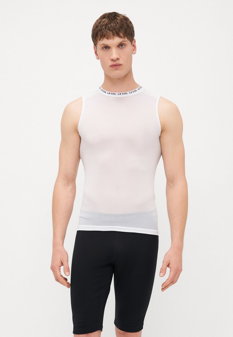Haut sans manches en maille blanc avec col rond haut et bande de logo noire, associé à un short noir ajusté jusqu'au genou.