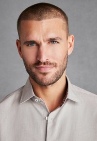 Jasnoszara, teksturowana koszula z delikatnym wzorem i kontrastowym, wzorzystym wnętrzem kołnierzyka. Posiada styl na guziki oraz kołnierz.