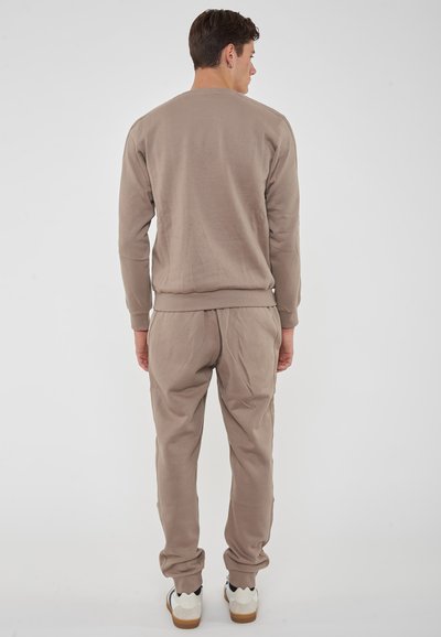 Felpa beige e pantaloni joggers coordinati. Tessuto morbido, polsini a coste, vita elastica. Sneakers con una combinazione di colori bianco e blu navy, suola graffiata.