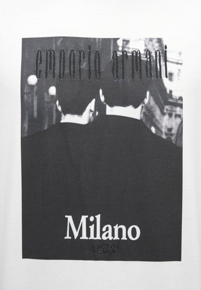 Biele tričko s čiernou grafickou potlačou dvoch postáv z profilu, s textom "emporio armani" a "Milano" v kontrastných farbách.