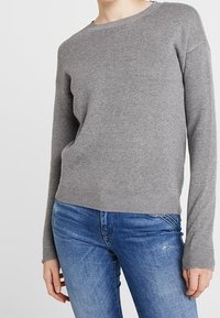 Gray knit sweater with a round neckline, ribbed cuffs and hem, paired with blue jeans. Soft texture, casual fit, and simple design.