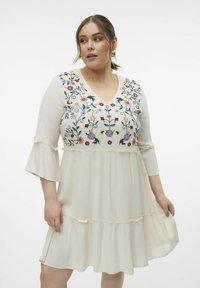 Vestido blanco hasta la rodilla con bordado floral alrededor del escote y mangas acampanadas; tiene un dobladillo en capas con volantes y está confeccionado en un tejido ligero.