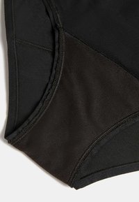 Biancheria intima nera con texture liscia, caratterizzata da materiali sovrapposti; una combinazione di tessuto opaco e leggermente lucido, con bordi cuciti.