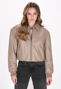 Beige læder bomberjakke med frontlynlås, krave og elastiske ærmer, kombineret med højtaljede sorte jeans. Blød tekstur, sporty design.